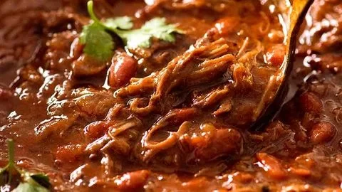 Bowl of shredded beef chili garnished with cilantro and lime
